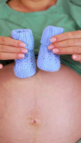 beautiful pregnant woman with baby shoes at home. pregnant woman preparing for motherhood, holding small baby shoes near belly. vertical video