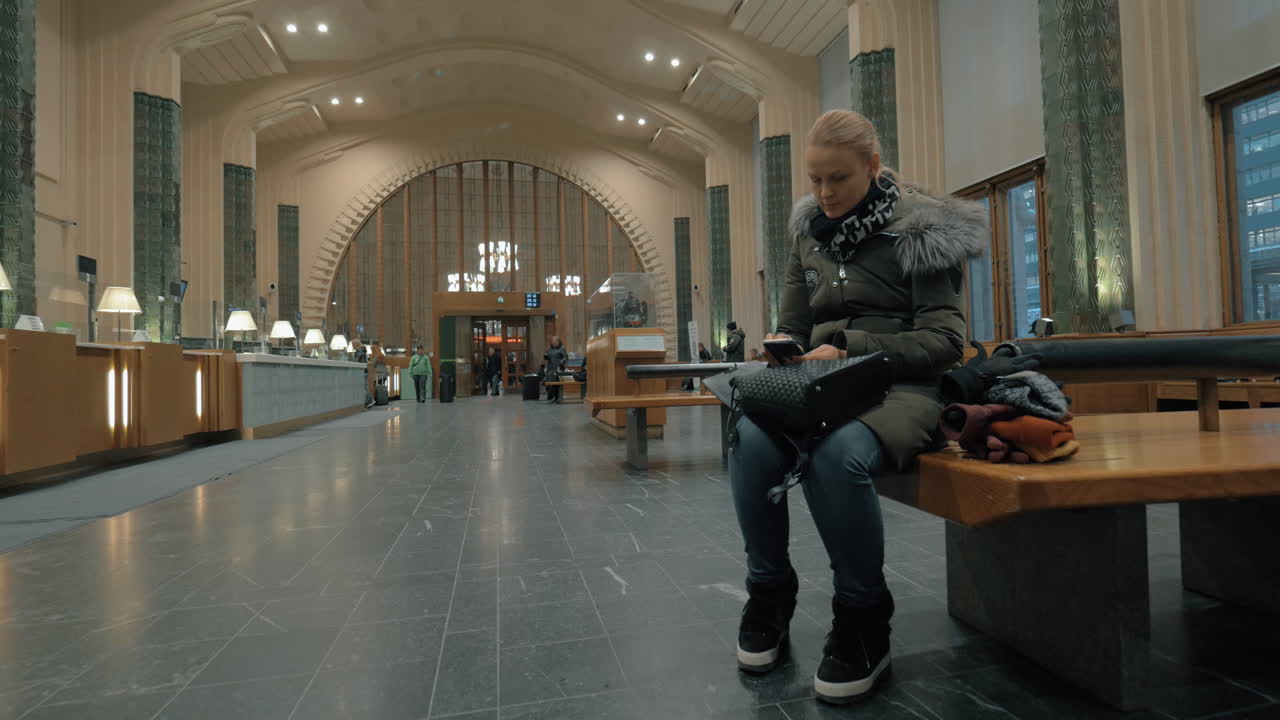 Kvinde venter i stationshallen og bruger smartphone