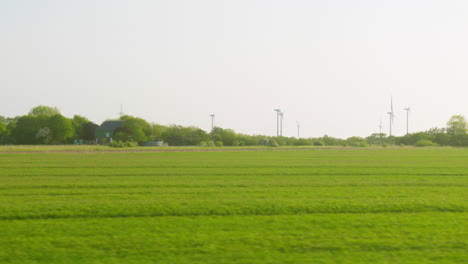 Windpark-Entlang-Der-Bahnstrecke:-Schöne-Aussicht-Auf-Grüne-Felder-In-Norddeutschland,-Vom-Fenster-Aus-Gesehen