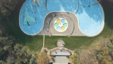 top down aerial of deserted outdoor swimming pool surrounded by forest