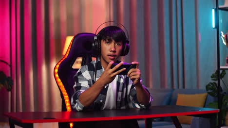 asian teen boy gamer smiling to camera and showing thumb up while playing video game on smartphone