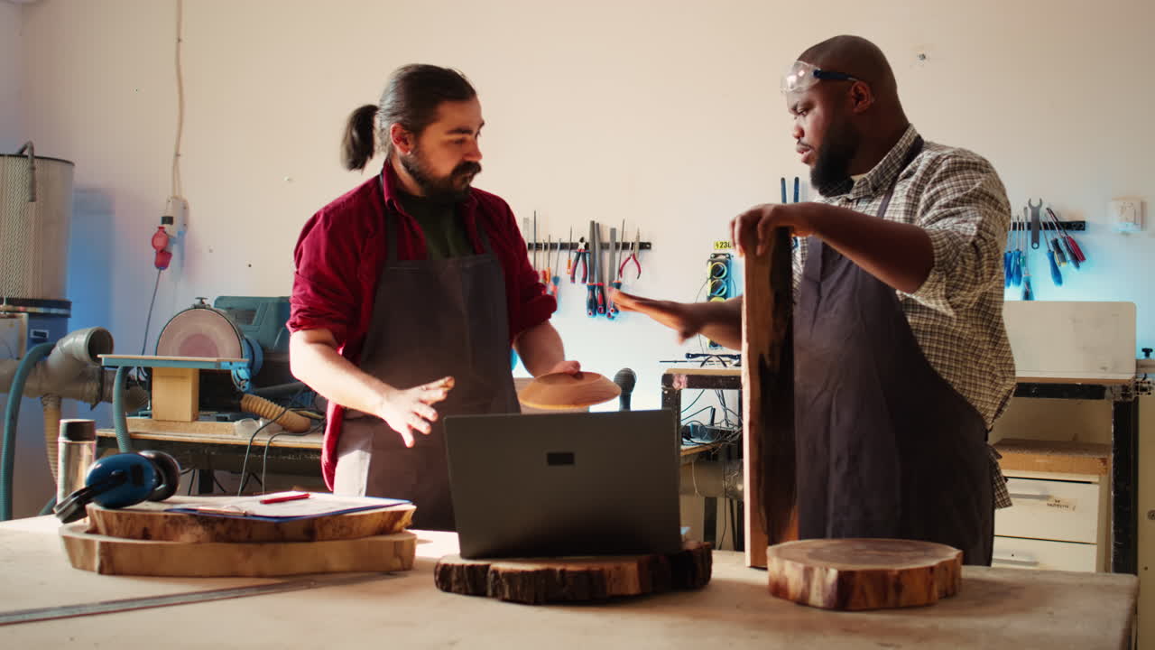 Woodworker looking over blueprints on laptop, brainstorming with colleague