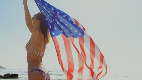 Side-view-of-young-Caucasian-woman-holding-a-American-flag-on-the-beach-4k