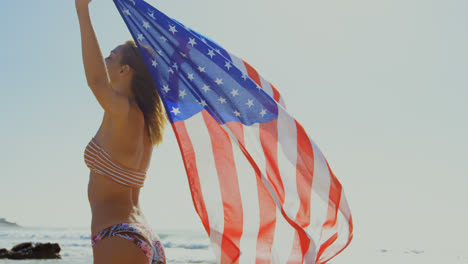 vista lateral de una joven mujer caucásica sosteniendo una bandera estadounidense en la playa 4k