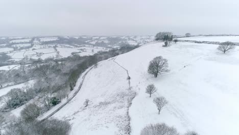 aerial forward tracking across vast english farmland covered in snow, with a hillside common in the foreground with a valley in the background