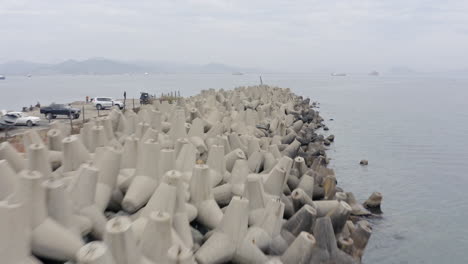 Volar-Sobre-Una-Línea-De-Rompeolas-De-Hormigón-Con-El-Muelle-En-El-Lado-Izquierdo-Y-La-Bahía-Con-Shsips-En-El-Fondeadero-En-El-Fondo