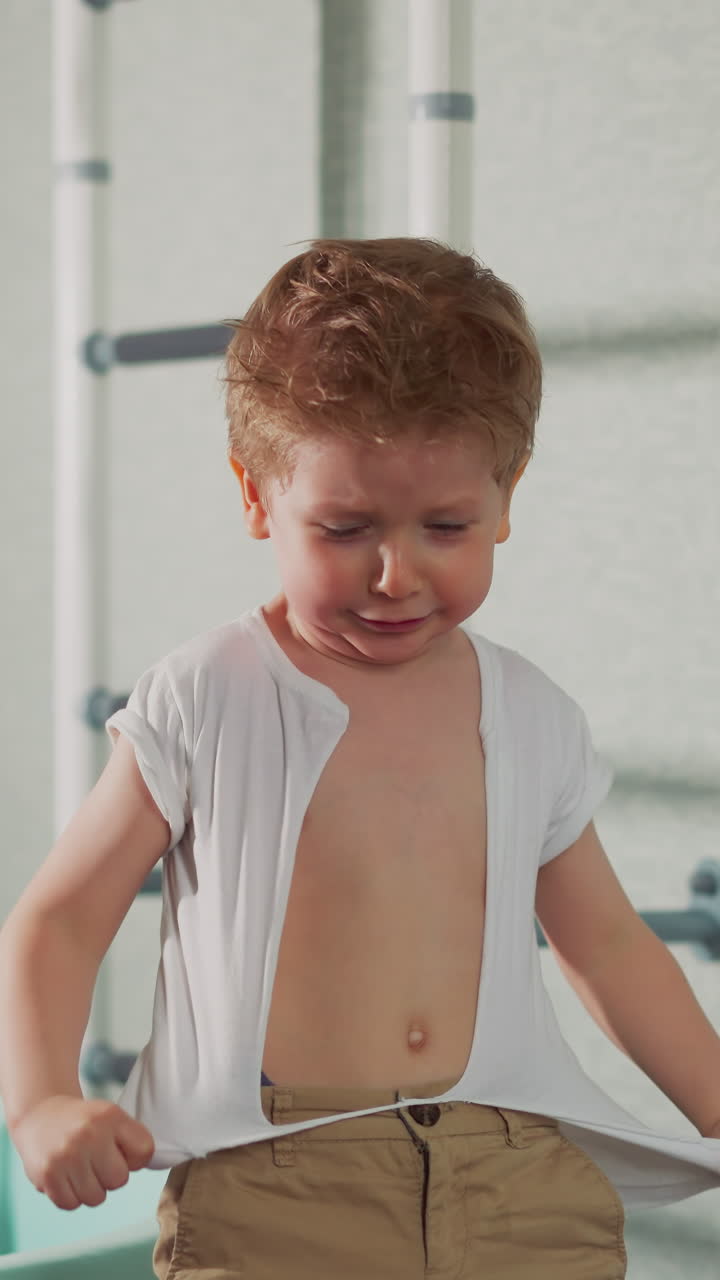 Naughty little boy tears white t-shirt on chest playing action movie hero slow motion. Toddler kid destroys clothes in home gym. Angry child emotions