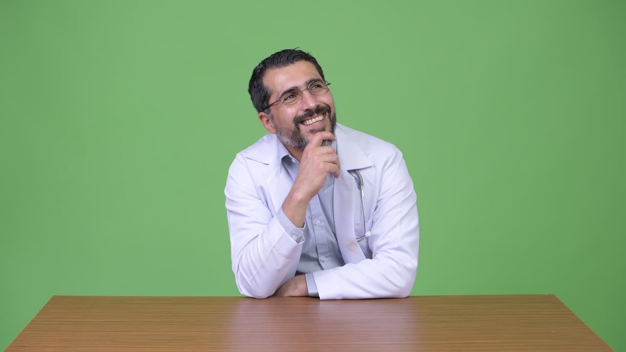 Handsome Persian bearded man doctor smiling while thinking