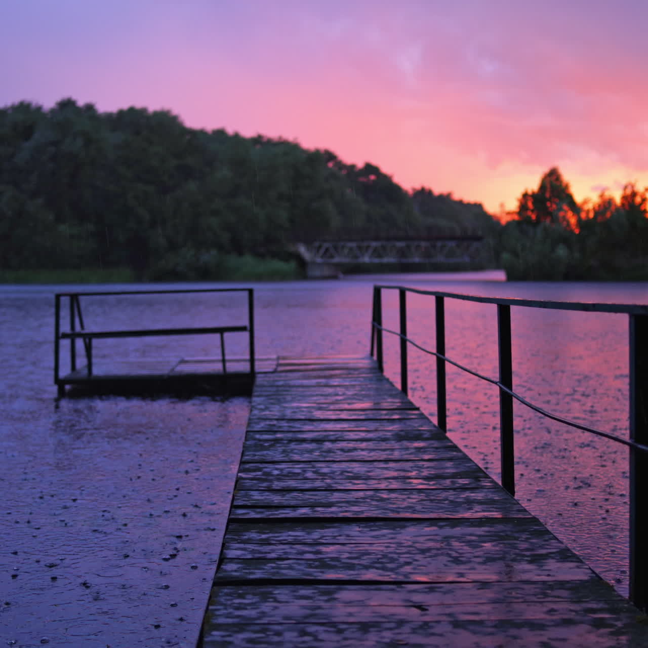 Empty wooden bridge over the river during the rain at sunset. The footbridge in the lake on the background of trees in the evening.