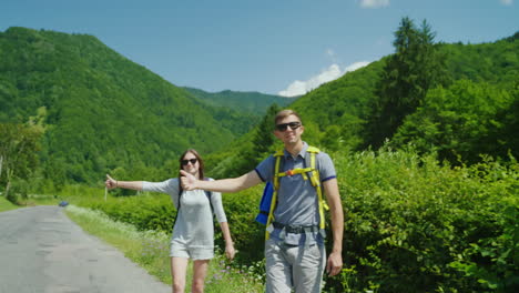 A-Young-Couple-Of-Tourists-With-Backpacks-Are-Voting-On-The-Road---They-Stop-Passing-Cars-Hold-Your