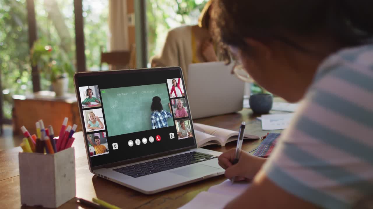 Schoolgirl using laptop for online lesson at home, with diverse teacher and class on screen