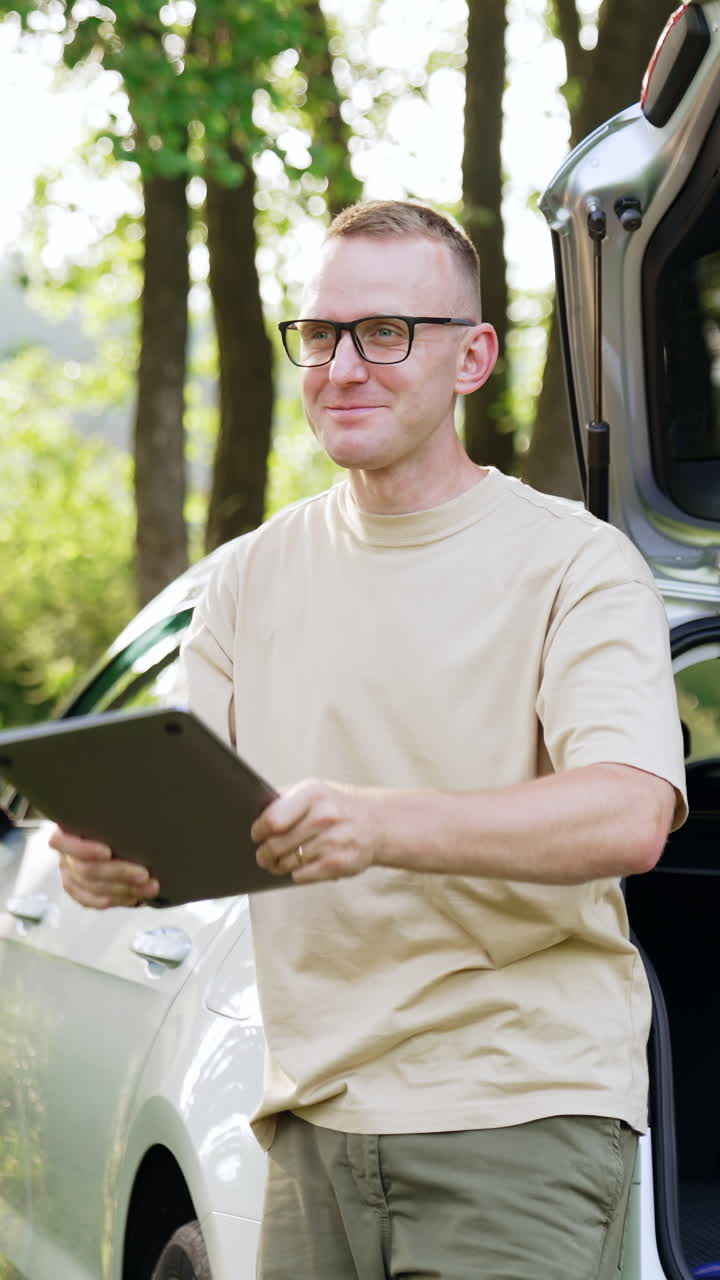 Serious Caucasian man holding a laptop in hands standing near the car outdoors. Male opens gadget and switches it on starting work. Vertical video
