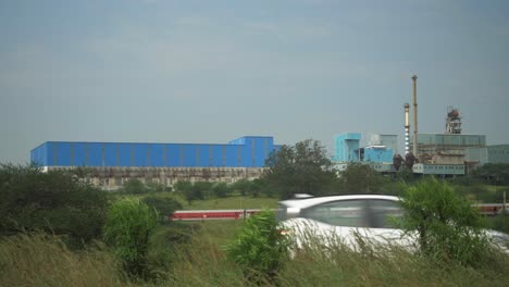 Toma-Estática-De-Ferrocarril-Y-Camión-Cruzándose-Entre-Sí-Con-Una-Planta-Industrial-En-El-Fondo