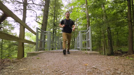 ein männlicher wanderer mit rucksack geht schnell die metalltreppe hinauf zur kamera in einer waldlandschaft, blick aus dem niedrigen winkel