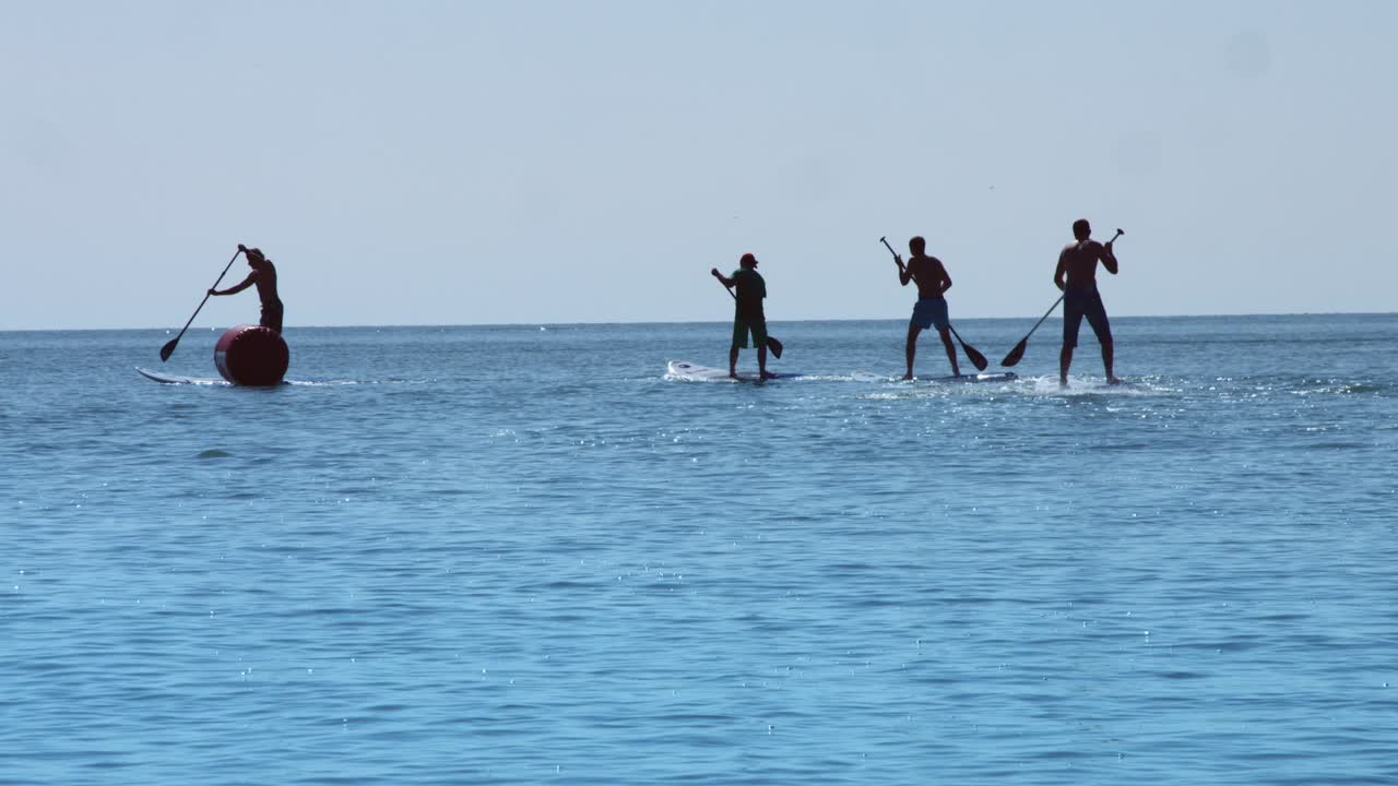 그룹 서퍼 남자가 서서 패들 보드를 타고 여름 휴가 동안 바다를 타고 있습니다.