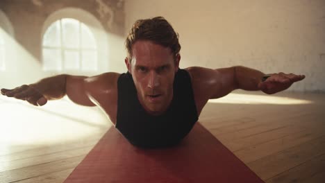 close-up shot of a male athlete in a black summer sports uniform doing exercises to strengthen the muscles of the back while lying on a special mat in a sunny brick hall