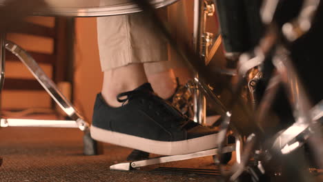 close up of an unrecognizable musician playing bass drum and pressing his foot on pedal during a band rehearsal in recording studio