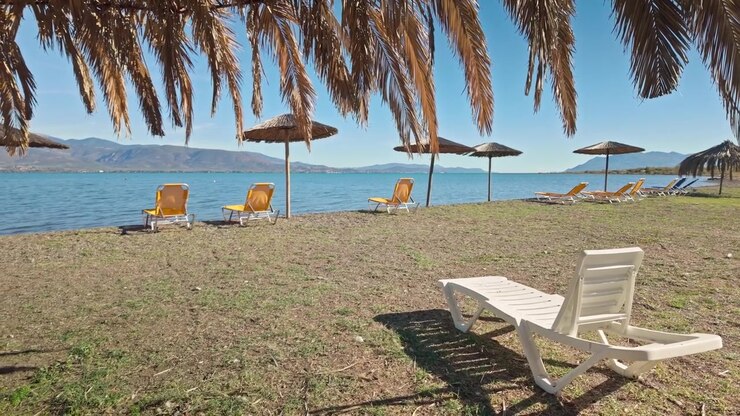 Spiaggia greca deserta con lettini vuoti e ombrelloni di foglie di palma.
