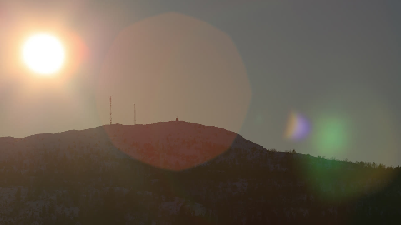 아름다운 렌즈 플레어가 사라지기 전에 산 능선을 따라 내려가는 태양의 망원 샷