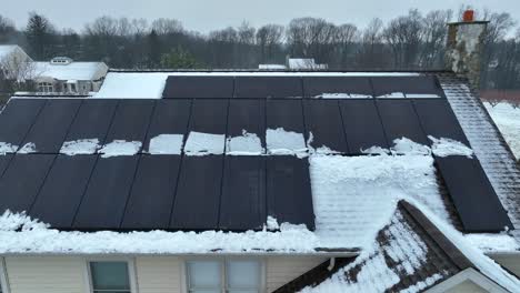 black solar panel units on icy and snowy roof of house in winter