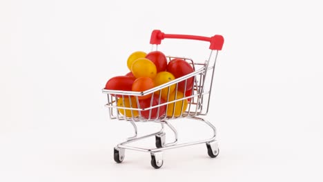 el carrito del supermercado lleno de tomates cereza rojos y amarillos. girando en la mesa giratoria. aislado en el fondo blanco. primer plano. macro.