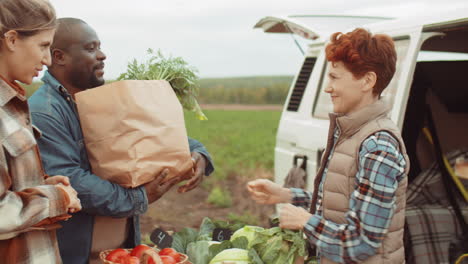 granjera alegre que vende verduras frescas a clientes multiétnicos