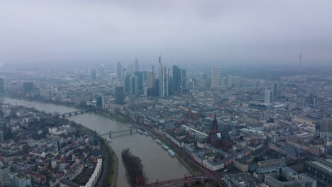 Vista-Aérea-Panorámica-Nebulosa-De-La-Ciudad.-Hitos-Históricos-De-Las-Modernas-Torres-De-Oficinas-De-Negocios.-Río-Que-Pasa-Por-Debajo-De-Los-Puentes.-Fráncfort-Del-Meno,-Alemania