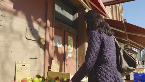 an attractive chinese woman examines ripe mangos at an outdoor fruit market on a cool spring day