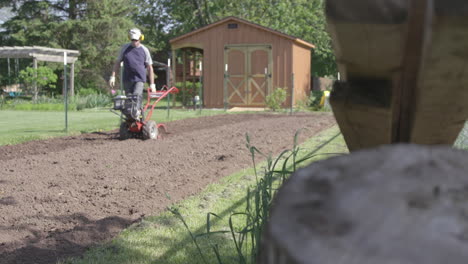 older gentleman prepares his garden for the spring by tilling the soil