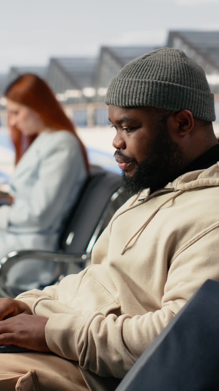 Vertical Video Black man digital nomad working on laptop in busy airport terminal lounge