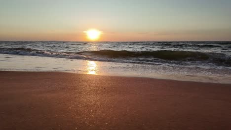 The-sun-sets-over-the-tranquil-Sea-of-Azov,-casting-golden-reflections-on-the-water-as-gentle-waves-lap-at-the-sandy-shore