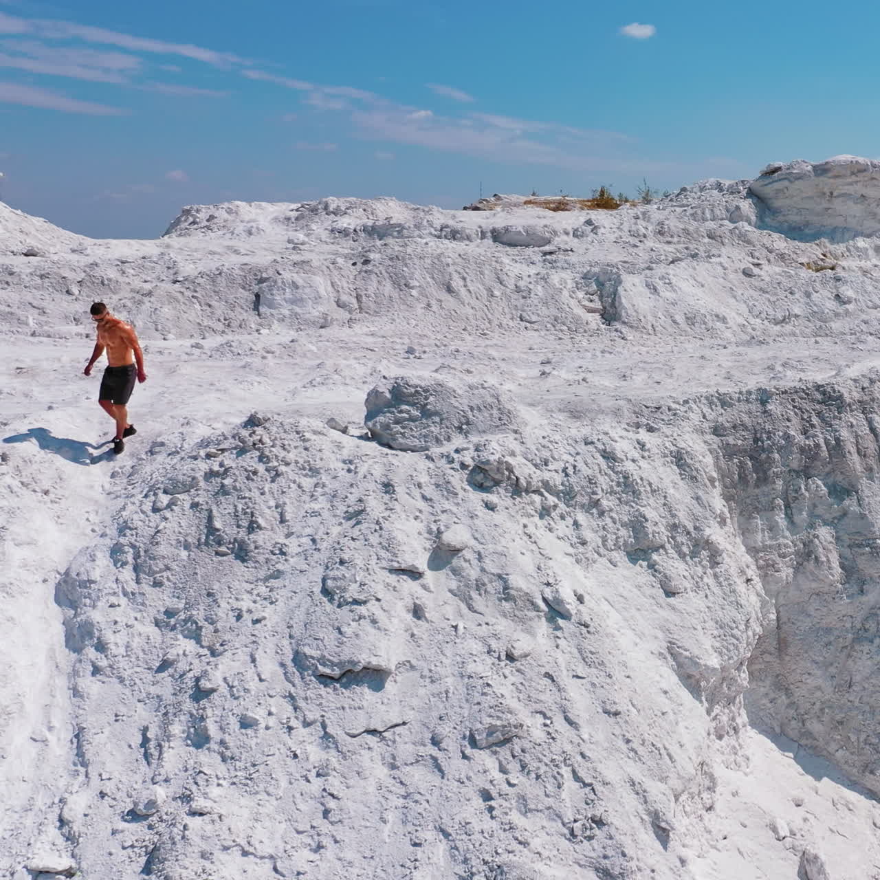 Sportsman on the mountainous area. Handsome man without shirt with muscular body walking on the top of the white hill. Aerial view.