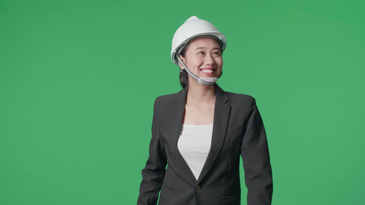 Smiling Asian Female Engineer With Blueprint Looking Around And Shaking Her Head While Walking In The Green Screen Studio