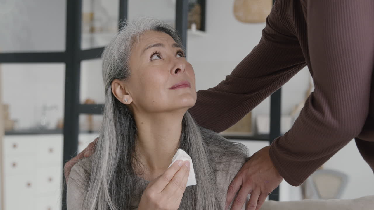 남편이 그녀를 위로하려고 노력하는 동안 슬픈 중년 여성이 울고 티슈로 눈물을 닦는다 1