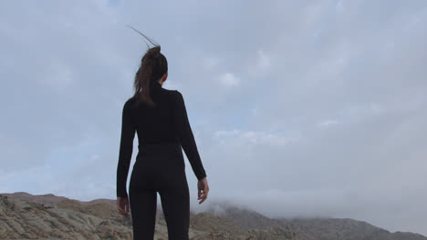 close-up of a woman in black standing strong in a mysterious desert at sunrise while the wind blows and moves her hair