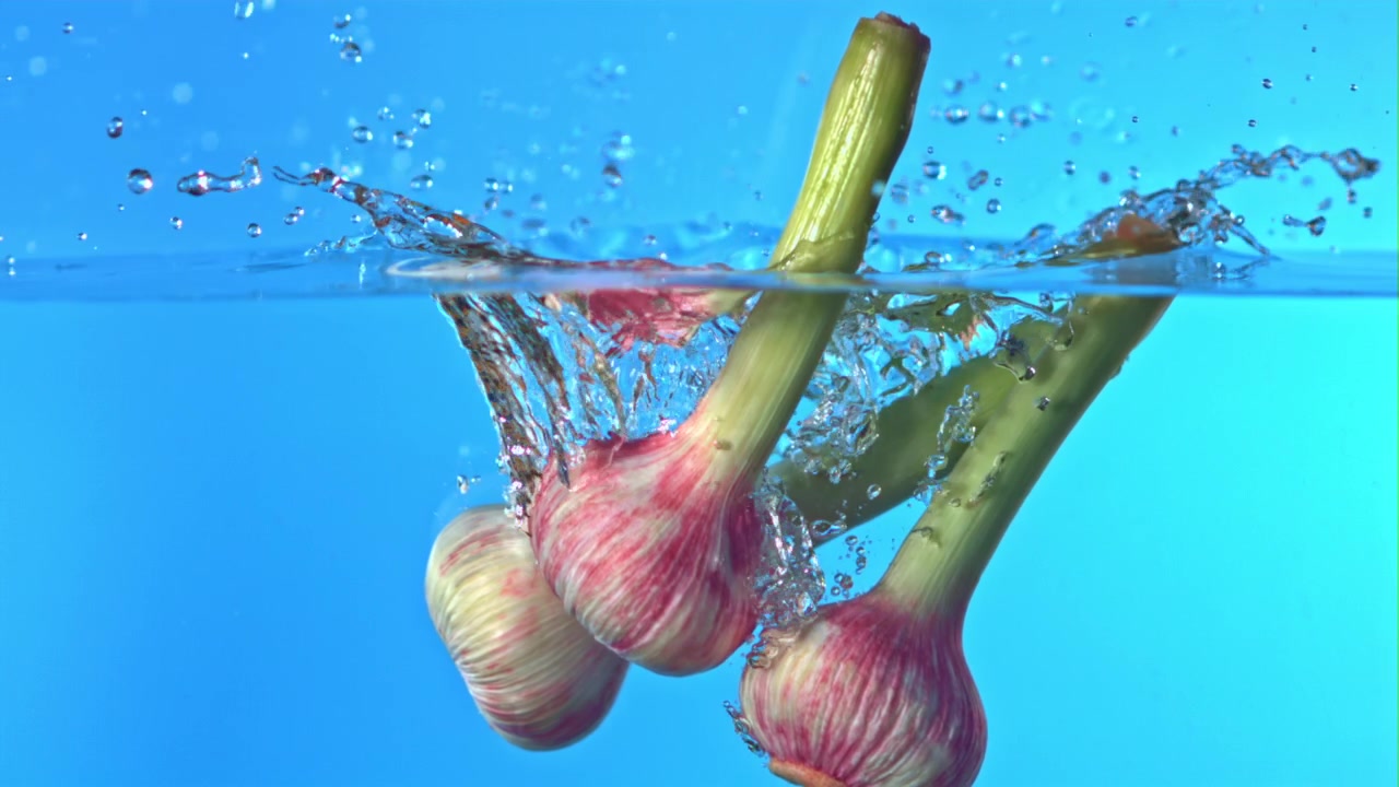 Slowmotion af frisk hvidløg, der falder ned i vand med sprøjt