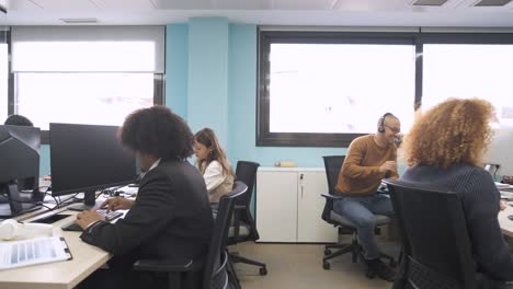 happy multiethnic colleagues discussing and working on computers in creative workspace