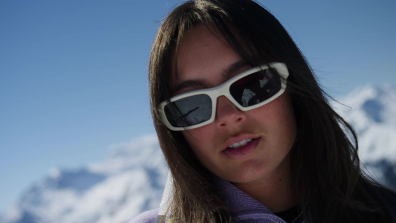 Young female skier carrying skis while enjoying panoramic mountain views in Verbier, Switzerland. Cinematic winter lifestyle footage featuring snow-covered peaks and alpine scenery in the Swiss Alps.