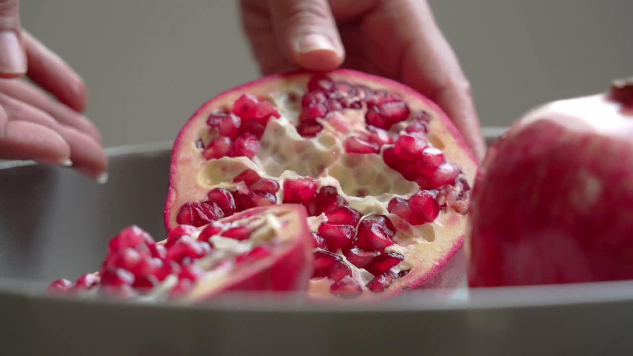 Nærbillede af et stort rødt granatæble, der åbnes, liggende på en hvid tallerken på et bord. Med sunde antioxidanter og hjertebeskyttende egenskaber.