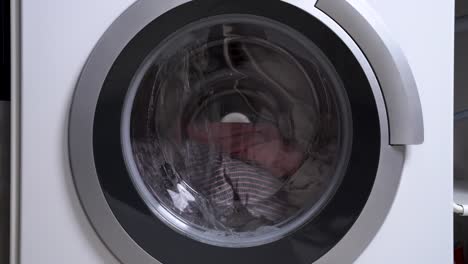 washing machine drum with laundries, where water begins to pour and rotation starts. the view through the front glass, indoors.