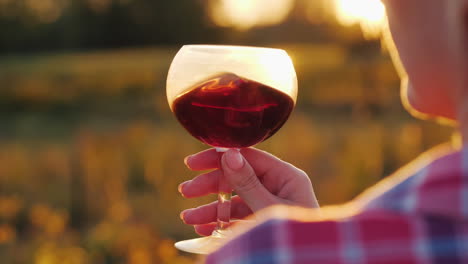 woman holds red wine by setting sun