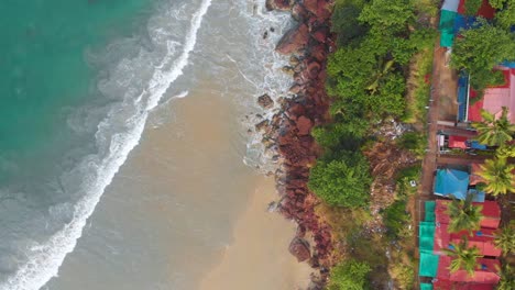 Aerial-top-down-view-of-calm-sea-waves-hitting-the-beautiful-beach-having-green-cliffs