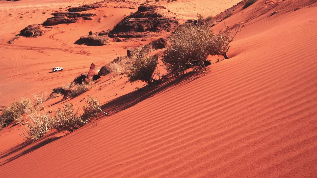 Side of the sand dune in the Wadi Rum desert, white jeep driving through below