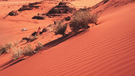 Side-of-the-sand-dune-in-the-Wadi-Rum-desert,-white-jeep-driving-through-below