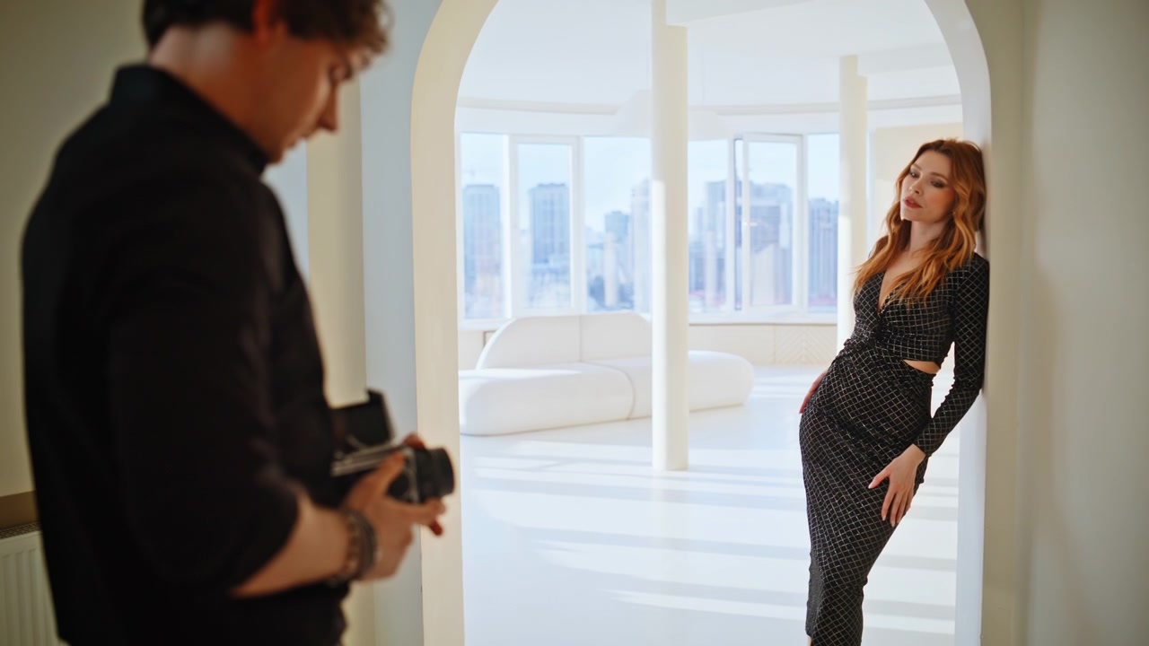 Modella di moda in posa con abito nero in appartamento di lusso. Fotografo che dirige il servizio fotografico