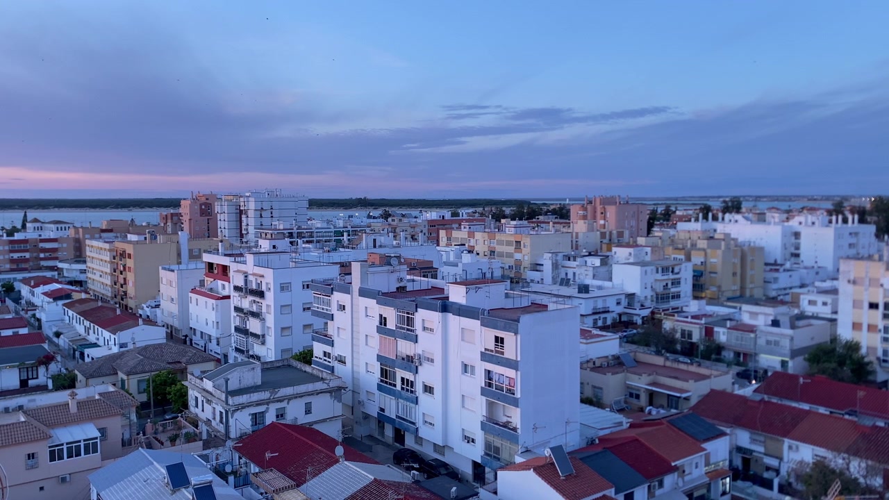 Cielo serale caldo su una città costiera in Spagna, che mostra edifici residenziali e un estuario fluviale che si fonde con il mare.