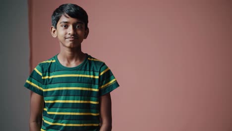 cheerful preteen boy with warm, genuine smile wearing striped t shirt, standing against soft pink studio backdrop, radiating youthful innocence and charm