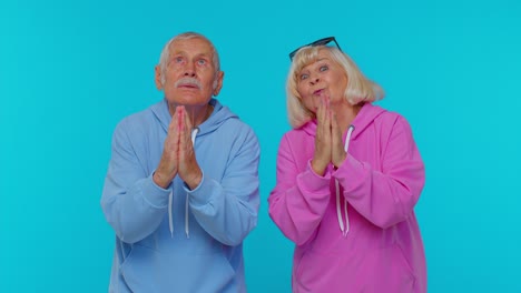 Senior-grandfather-grandmother-in-sweatshirts-praying,-looking-upward,-making-wish,-begging-apology