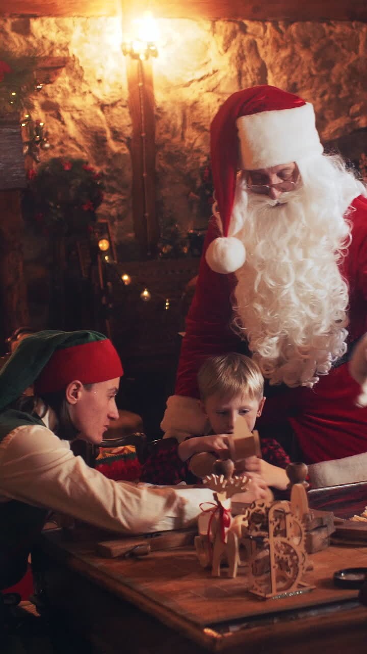 Santa Claus and elves are playing with children with wooden toys while sitting at a table in the New Year's residence. View from the street through the window. Vertical video