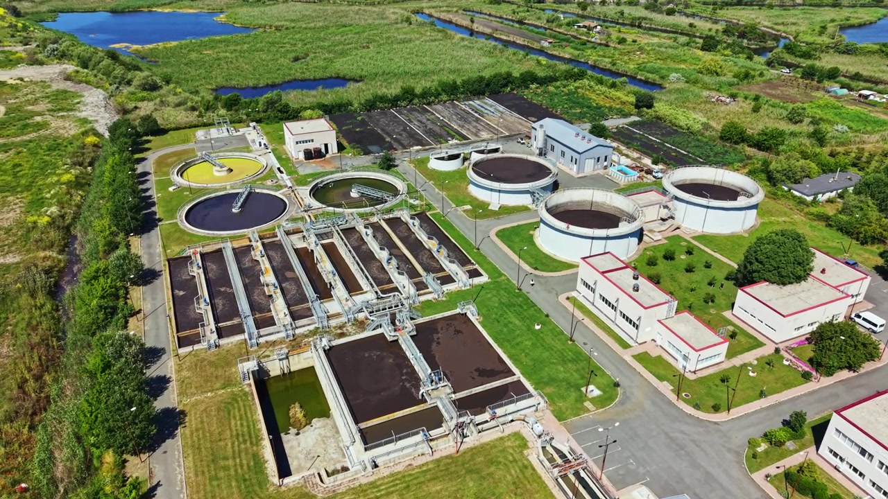 Water treatment facility at a riverbank with different processing units and green spaces during daylight